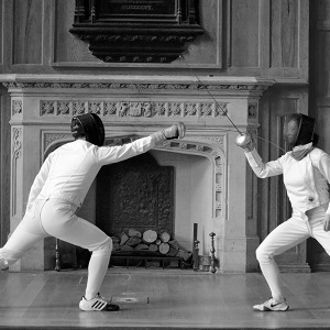 Two fencers fight in front of a fireplace