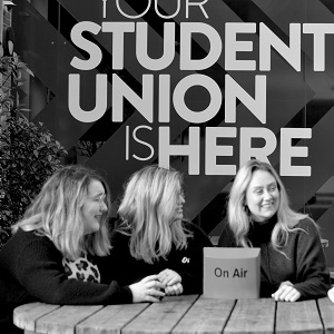 Queen's radio managers chat at a table in a black and white photo