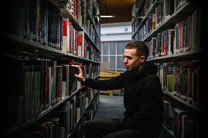 Student at shelves in the library selecting a book