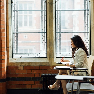 Student sits by a large window, alone, in the graduate centre