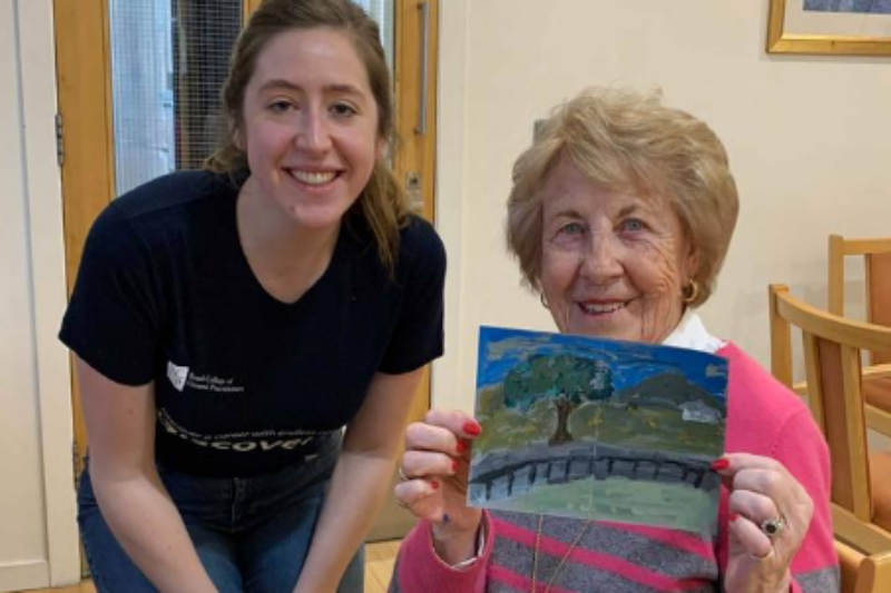 Young GP society students smiles beside an elderly woman holding a picture up