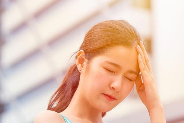 Woman touches her head in pain in the sun