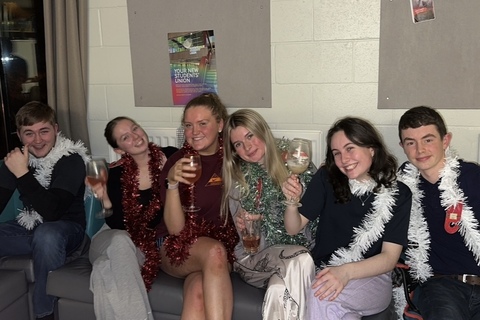 Six students sit together covered in tinsel at accommodation Christmas party