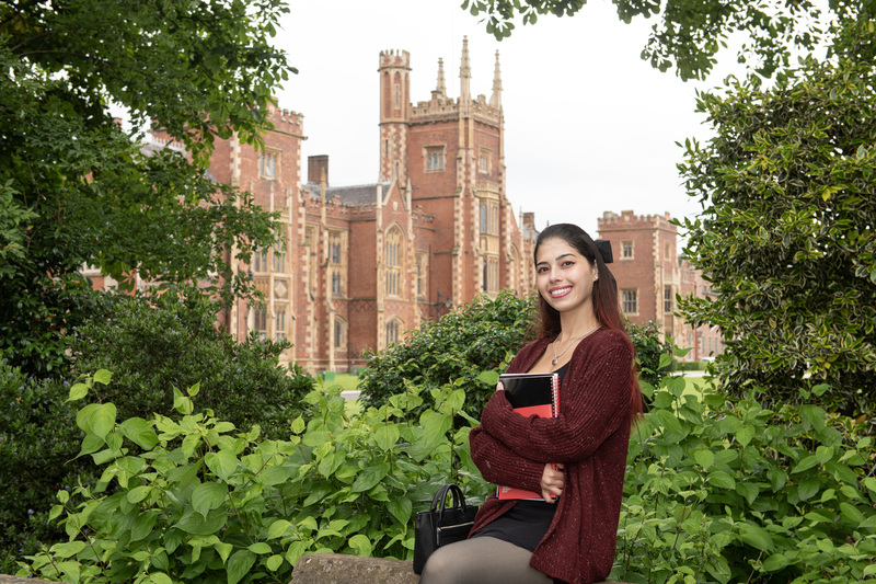 Female student poses in front of the Lanyon holding textbooks