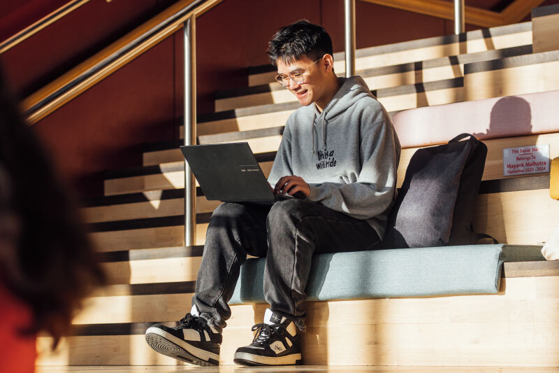 Student Bryan works on laptop on steps of One Elmwood