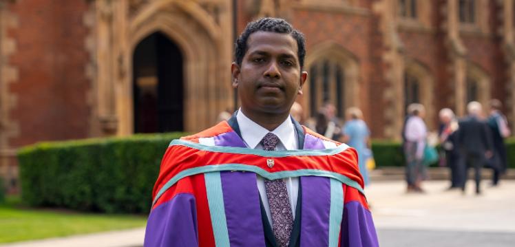 Graduate Ebenezer Veerasingam stands in academic robes outside Queen's University