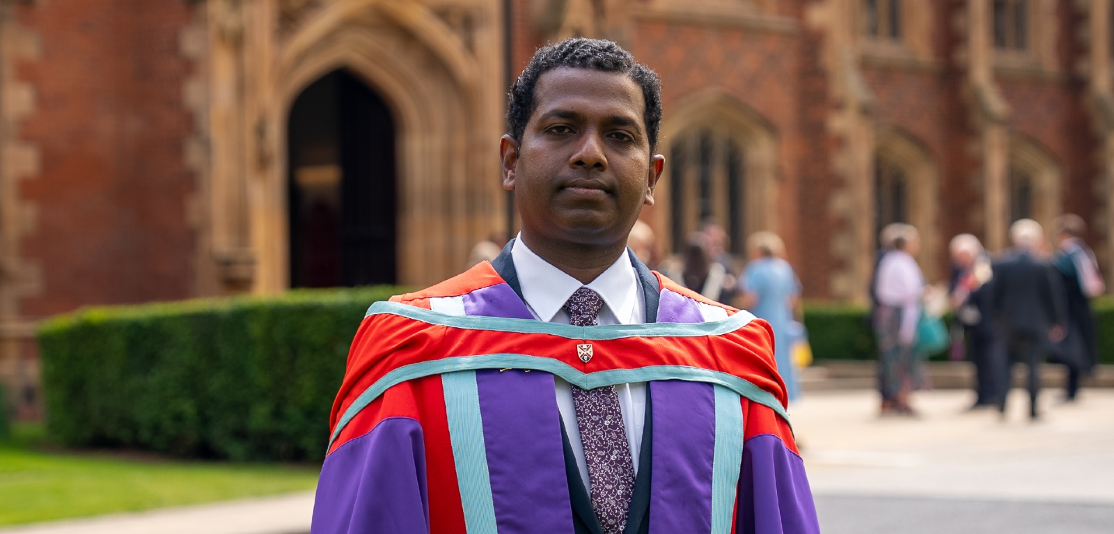 Graduate Ebenezer Veerasingam stands in academic robes outside Queen's University
