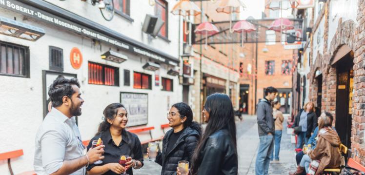 Four students stand together under umbrella display in Commercial Court