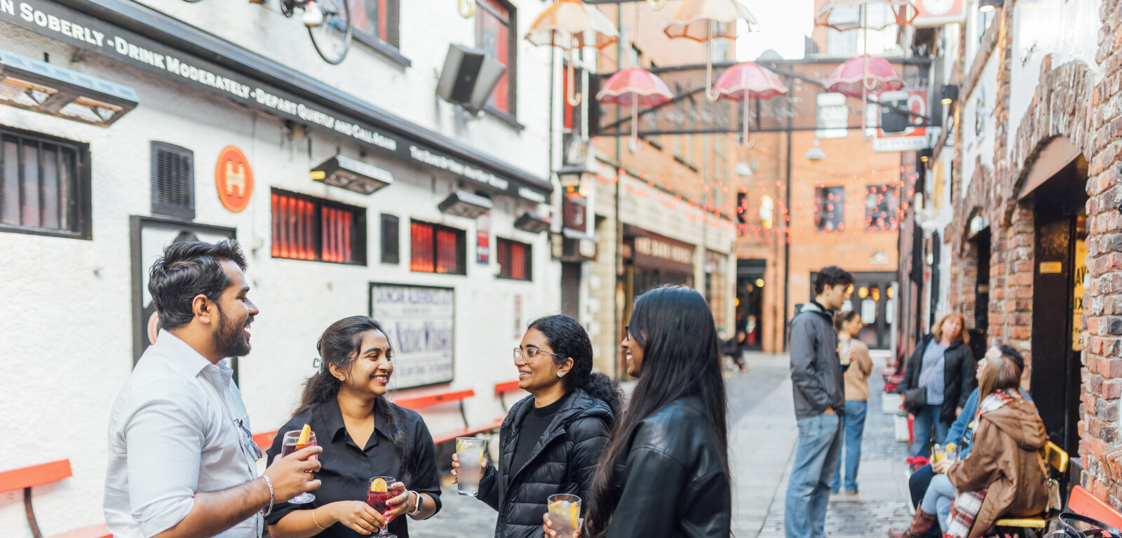 Four students stand together under umbrella display in Commercial Court