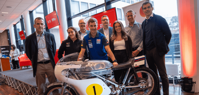 A group of people photographed in front of a motorbike at Queen's University