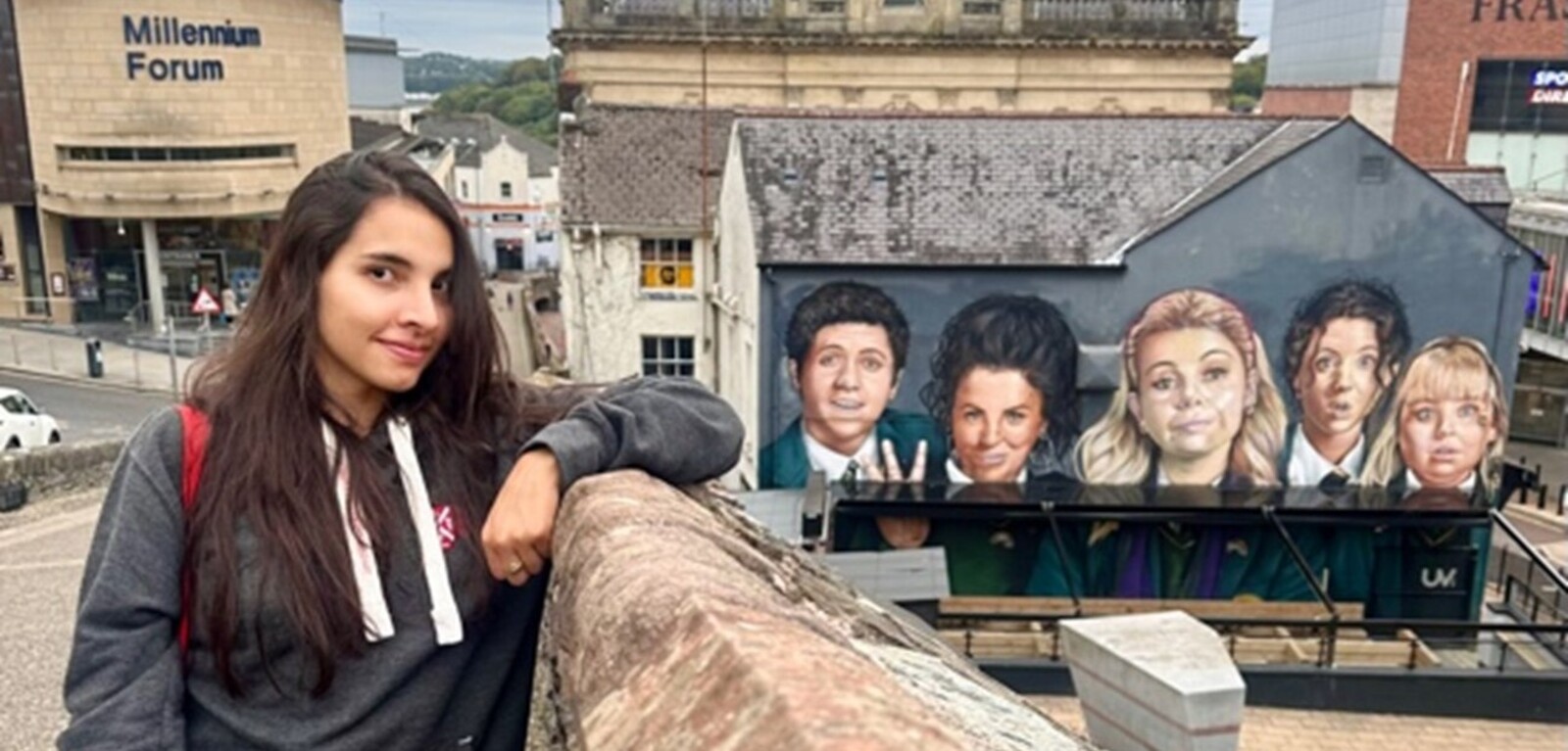 Student Isa standing in front of the Derry Girls mural in Derry