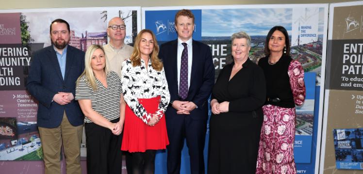 A group of people stand posed in front of banners in a community hall looking towards the camera.