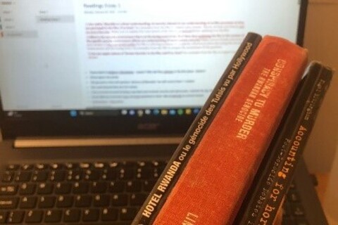 Student holding 3 library books with laptop in background