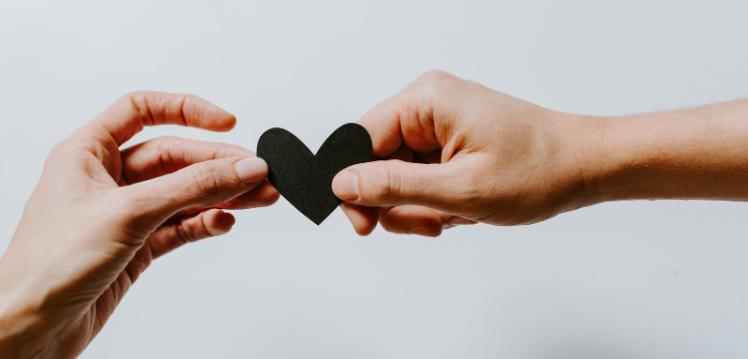 Two hands holding a black paper heart cut out