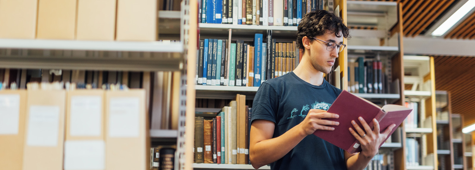Student Lucas reads book in front of bookcases in the McClay Library