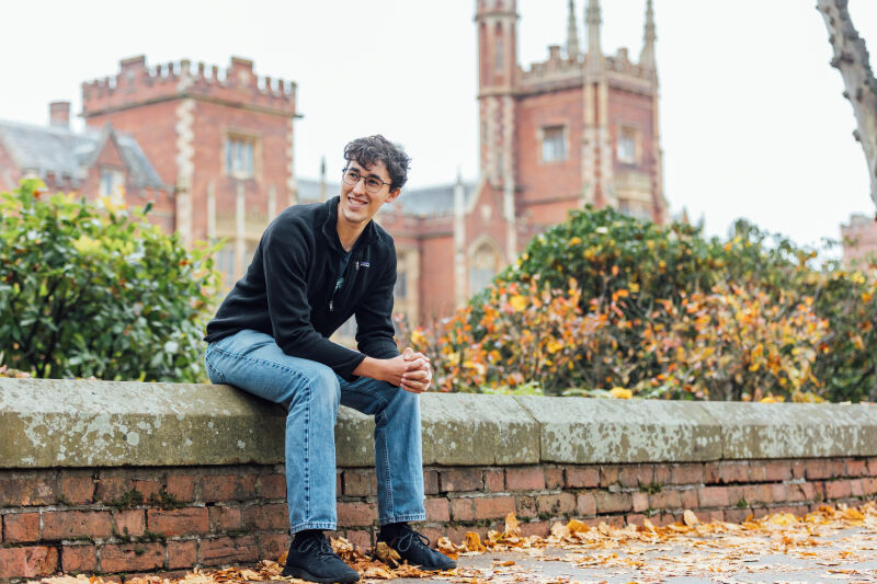 Student Lucas sits on wall in front of Lanyon Building