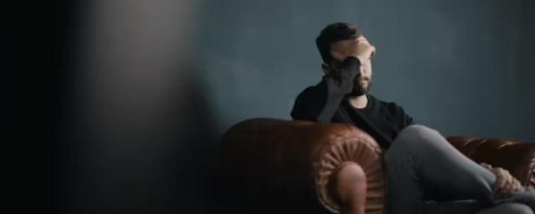 Man sitting on sofa with head leaning into his hand