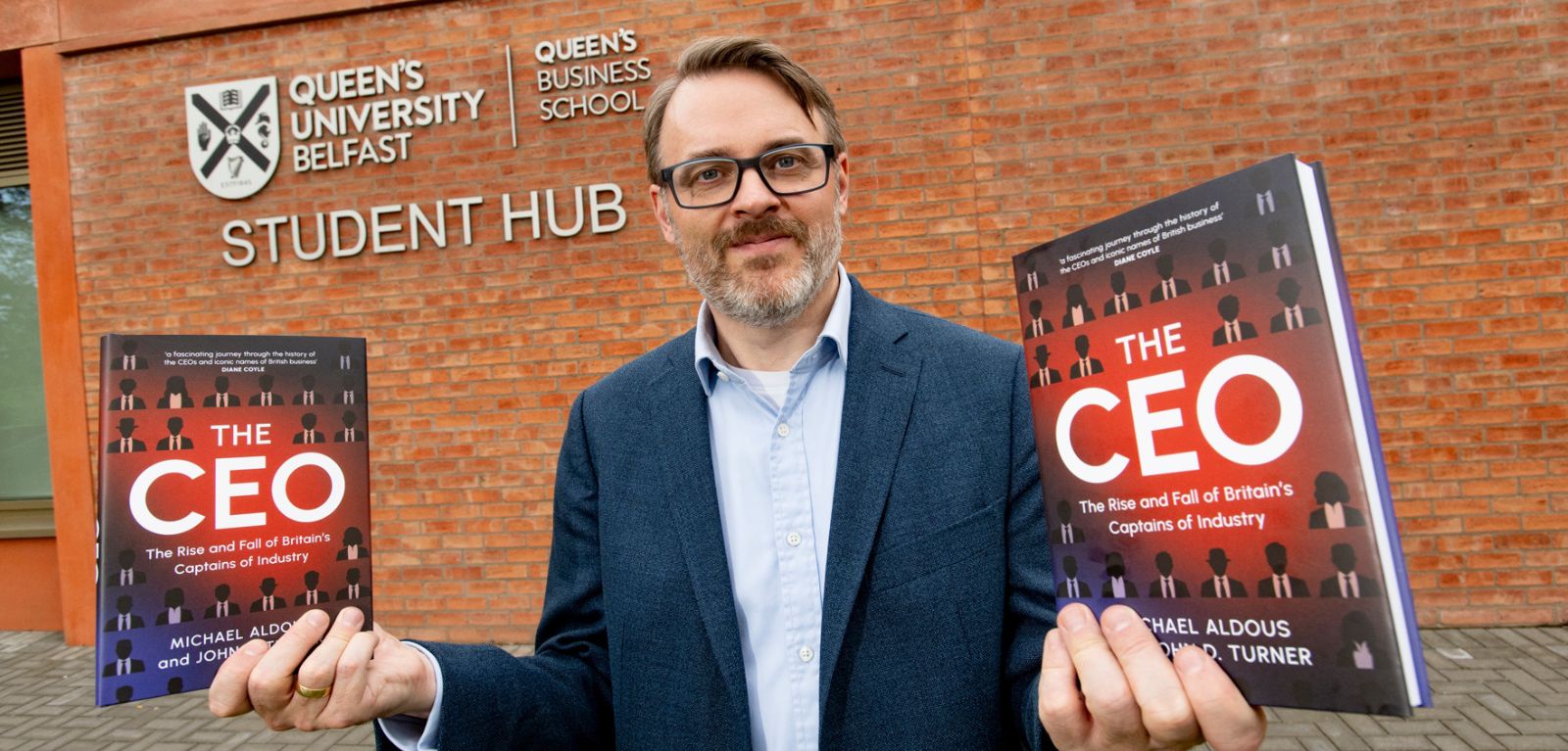 Man holding two books infront of a red brick building