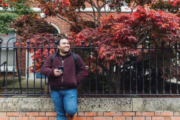 Student Miguel stands against metal fence on University Road