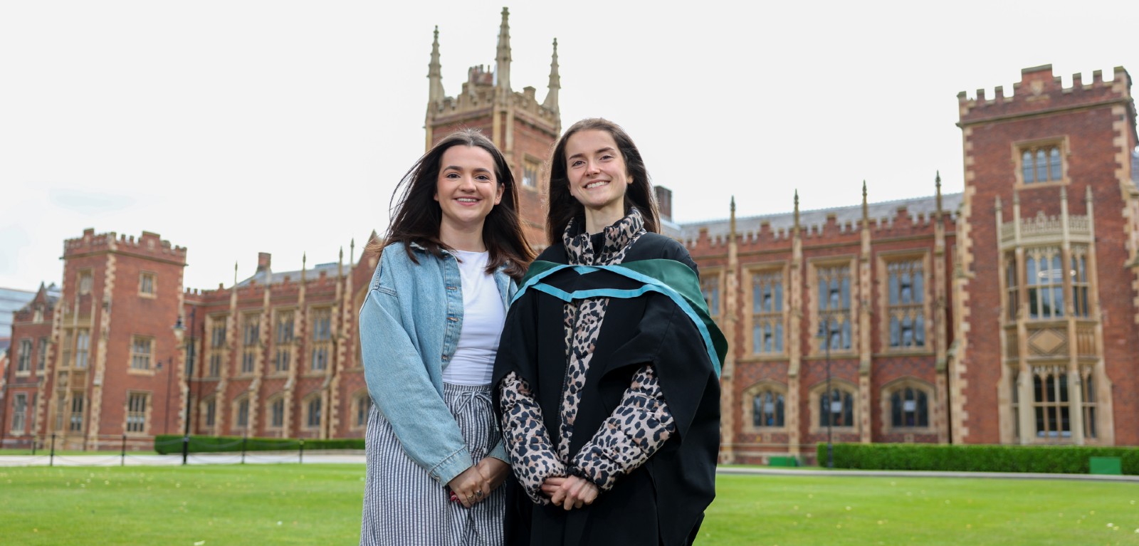 A university graduate and her sister stand in the grounds of Queen's University Belfast smiling and looking at the camera