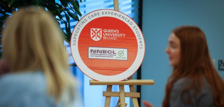 A university award sits in focus on an easel, two students sit in the foreground out of focus