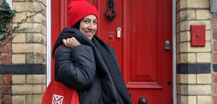 Student standing in front of red door holding red tote bag