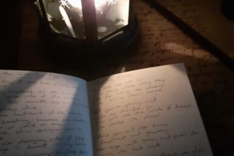 Book of handwritten poetry on table beside light