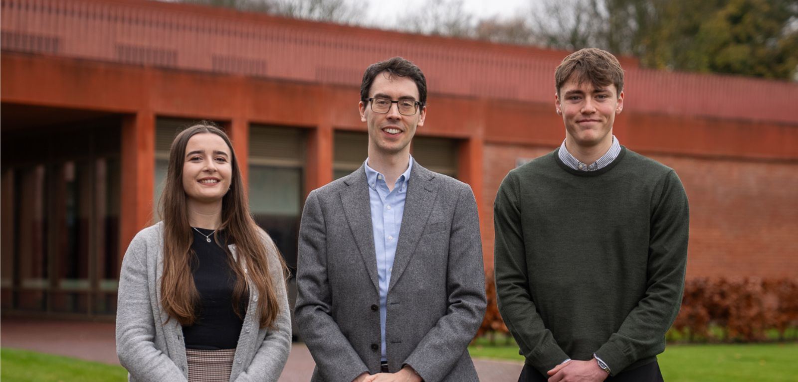 Three researchers standing in front of Queen's Business School