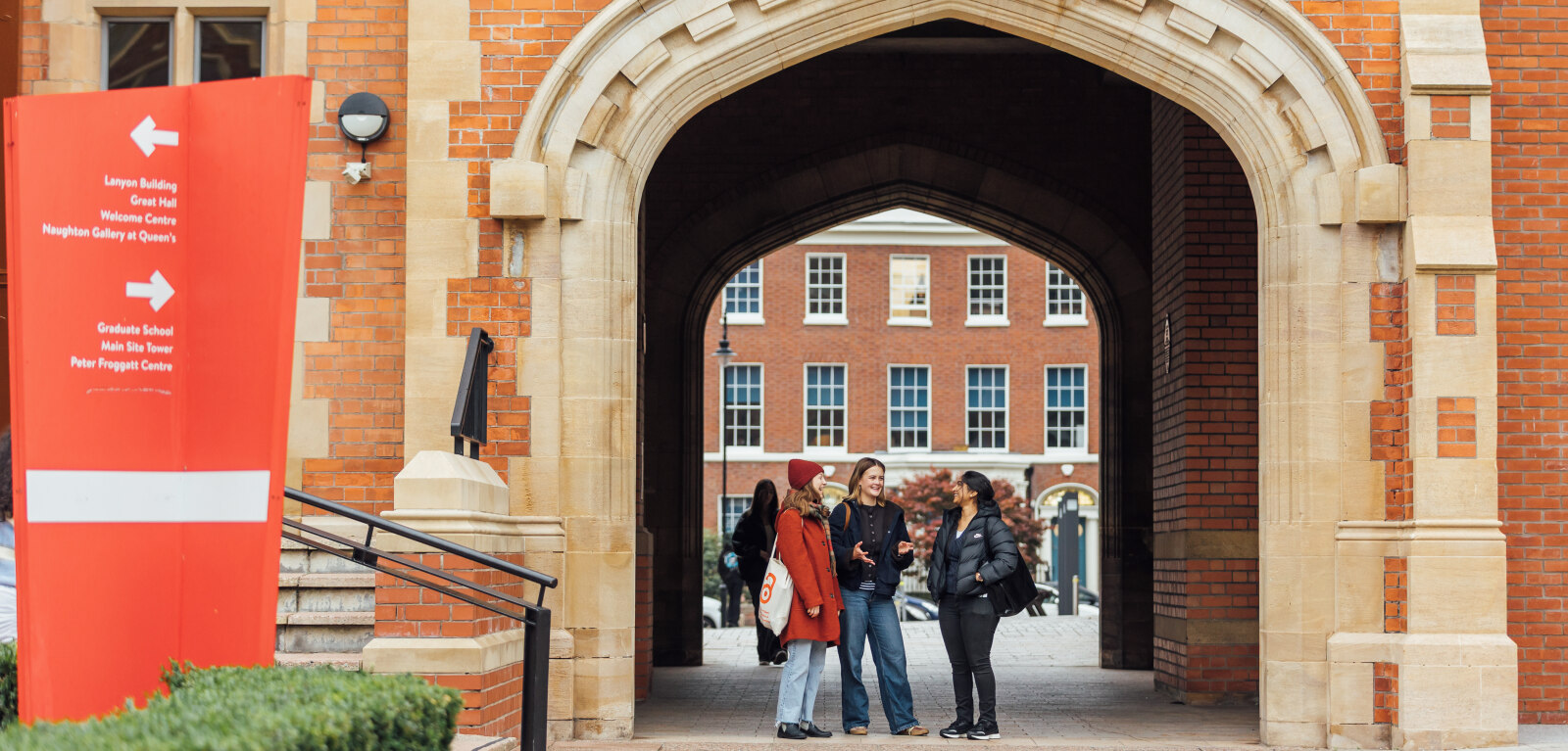 Three female students standing under arch in the quad