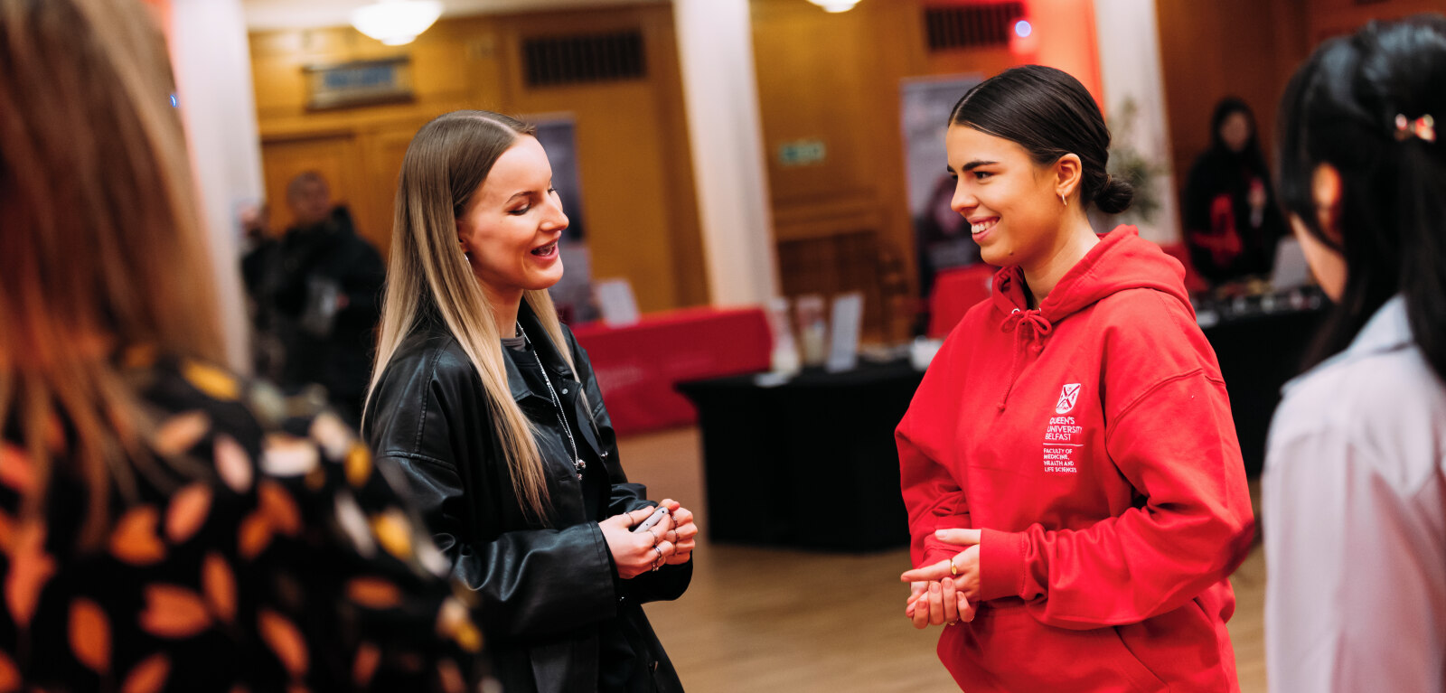 Two students talking, one wearing a read QUB hoodie