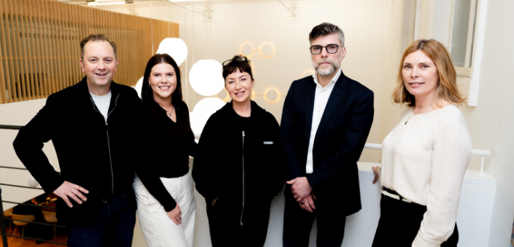 A group of people stand posed in a brightly lit room looking towards the camera.