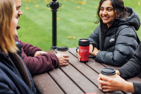 Student Sanjana sitting on bench in the Quad holding a QUB coffee flask