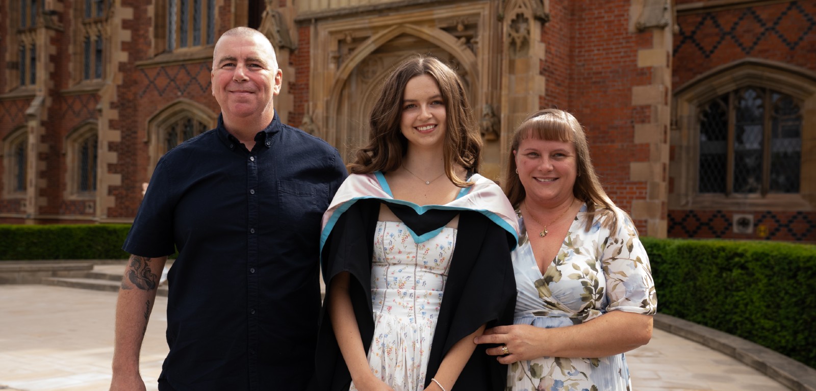 A graduate stands in between her mum and dad outside Queen's University Belfast