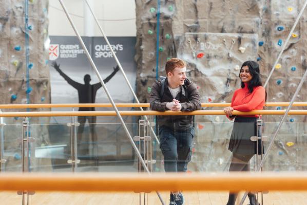 Students Sreyashi and Conor stand in front of climbing wall in the PEC