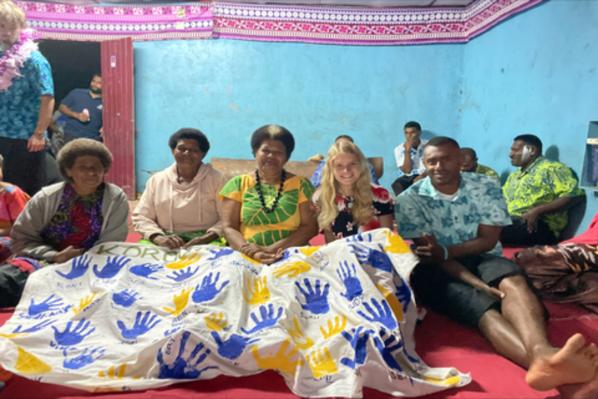Student sitting with group of Fiji villagers