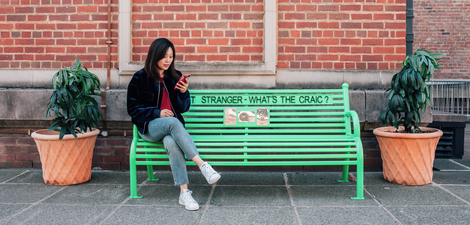 Student sitting on a green bench while looking at their phone