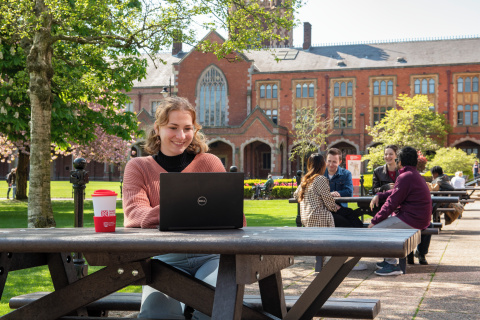 Student sitting in the Quad with coffee and laptop