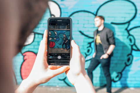 Student taking photo of another student standing against a wall