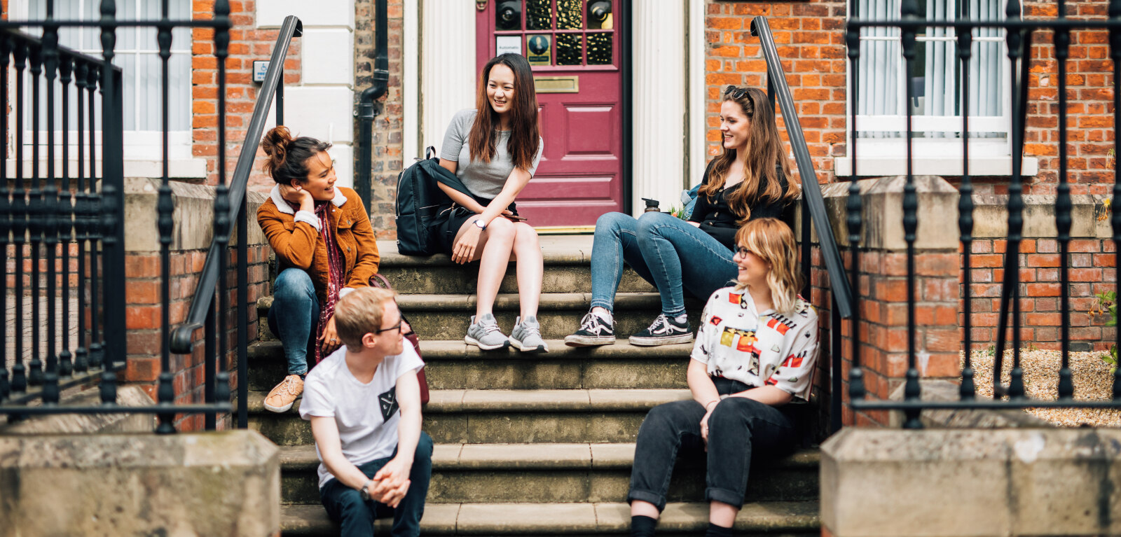 Group of five students laughing together while sitting on steps of Queen's campus building