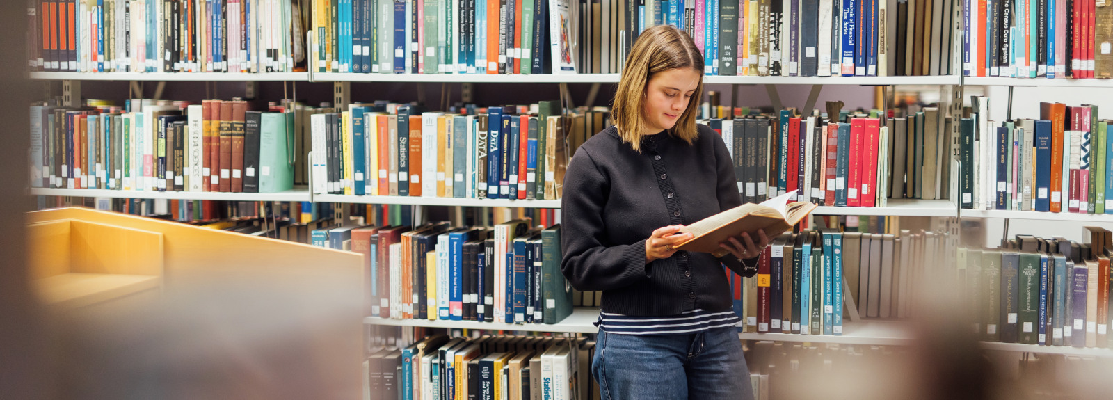 Student Tessa reads book in front of bookcase in the McClay Library