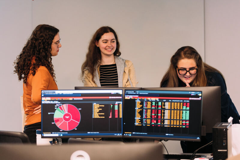 Three students stand in front of computer on offer holder day