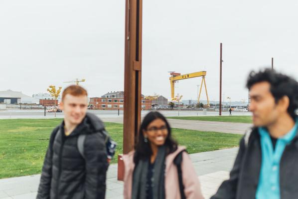 Three students walk down Titanic slipways with yellow crane in background