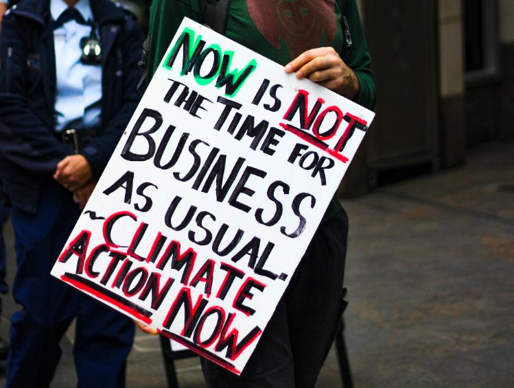 A placard which says 'Now is not the time for business as usual - Climate Action Now'