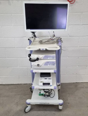 A picture of the Bronchoscopy: Olympus against a white brick wall on a concrete floor. The screen is black as the machine is not in use.