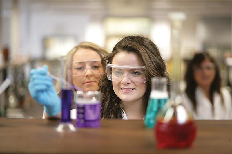 female student in lab coat extracting a purple liquid from a beaker with a pipette