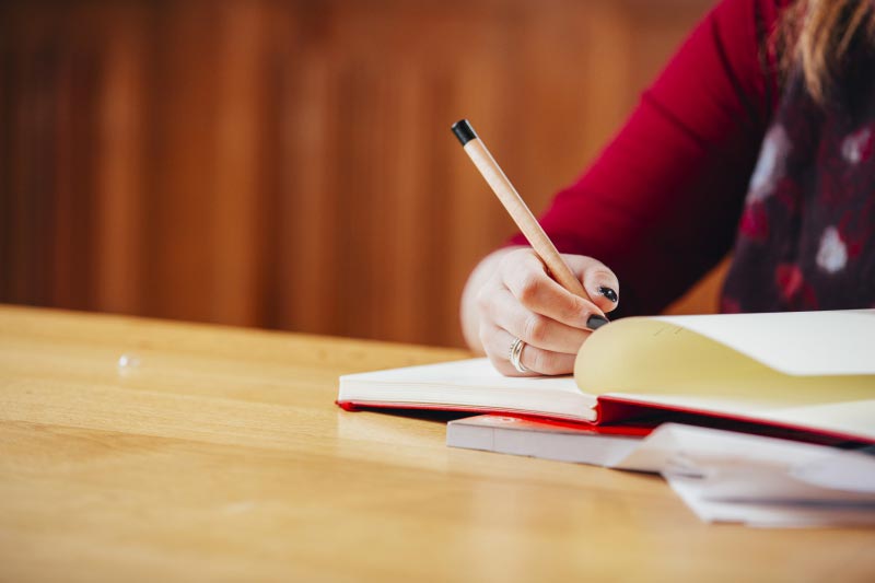 close up of female student taking notes in a red notebook