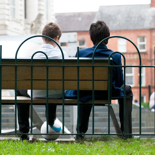 image of two boys wearing differenct school uniforms sitting on a bench 