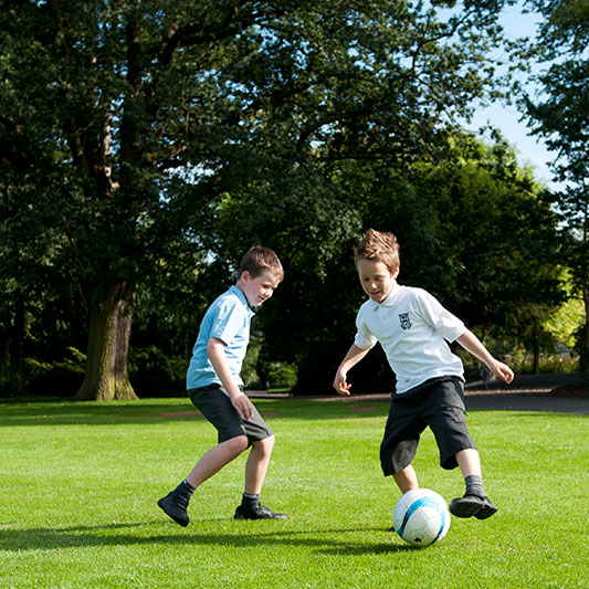 image of two primary school boys wearing different uniforms playing football in a park
