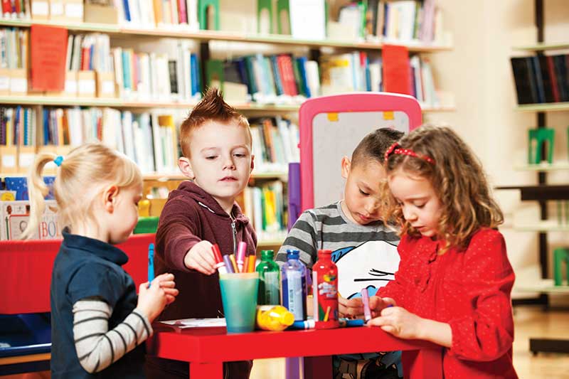 four early years children colouring-in around a table in a school setting