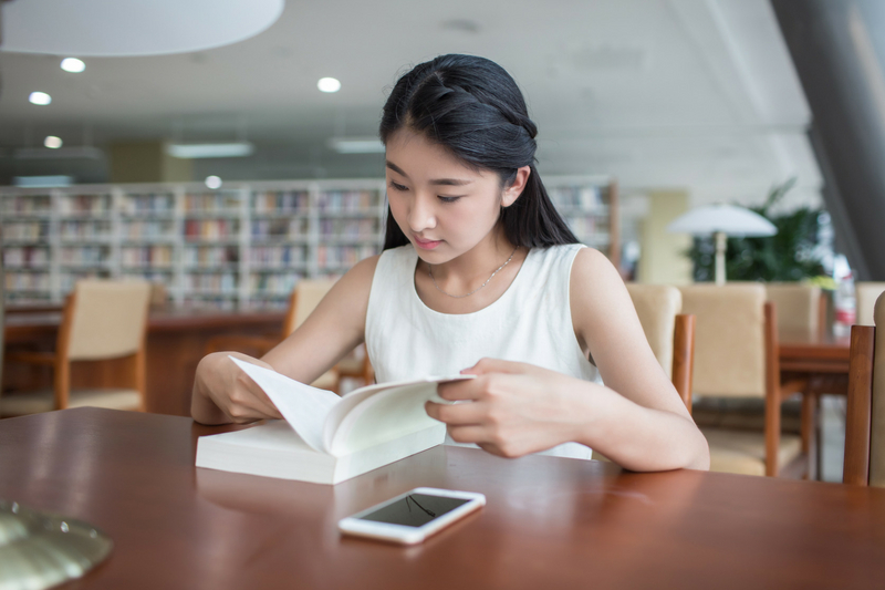 female student reading book in library